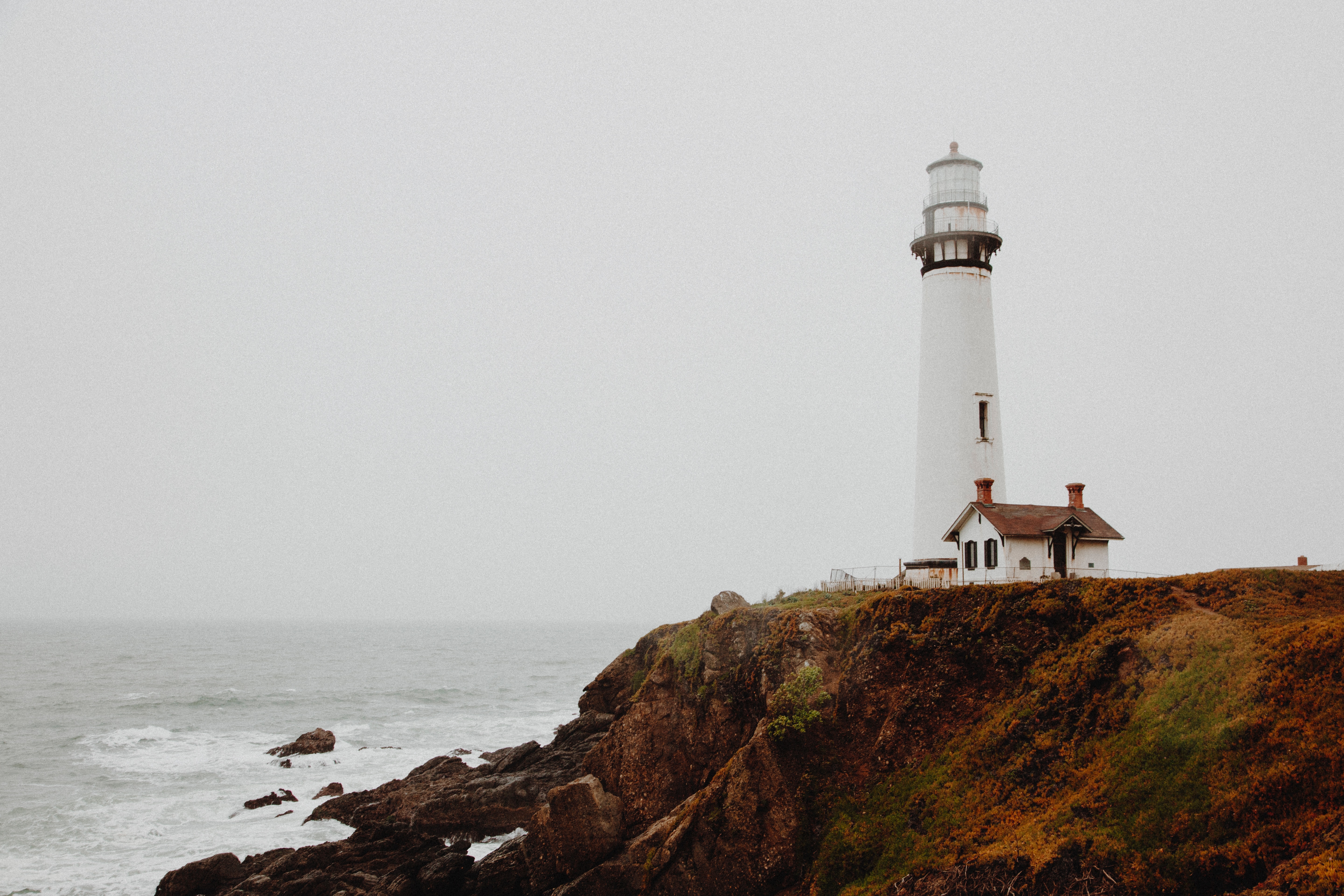A lighthouse on a rocky ocean shore in overcast skies