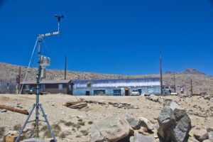 Weather monitoring equipment stands near a small research station in a barren, rocky landscape.