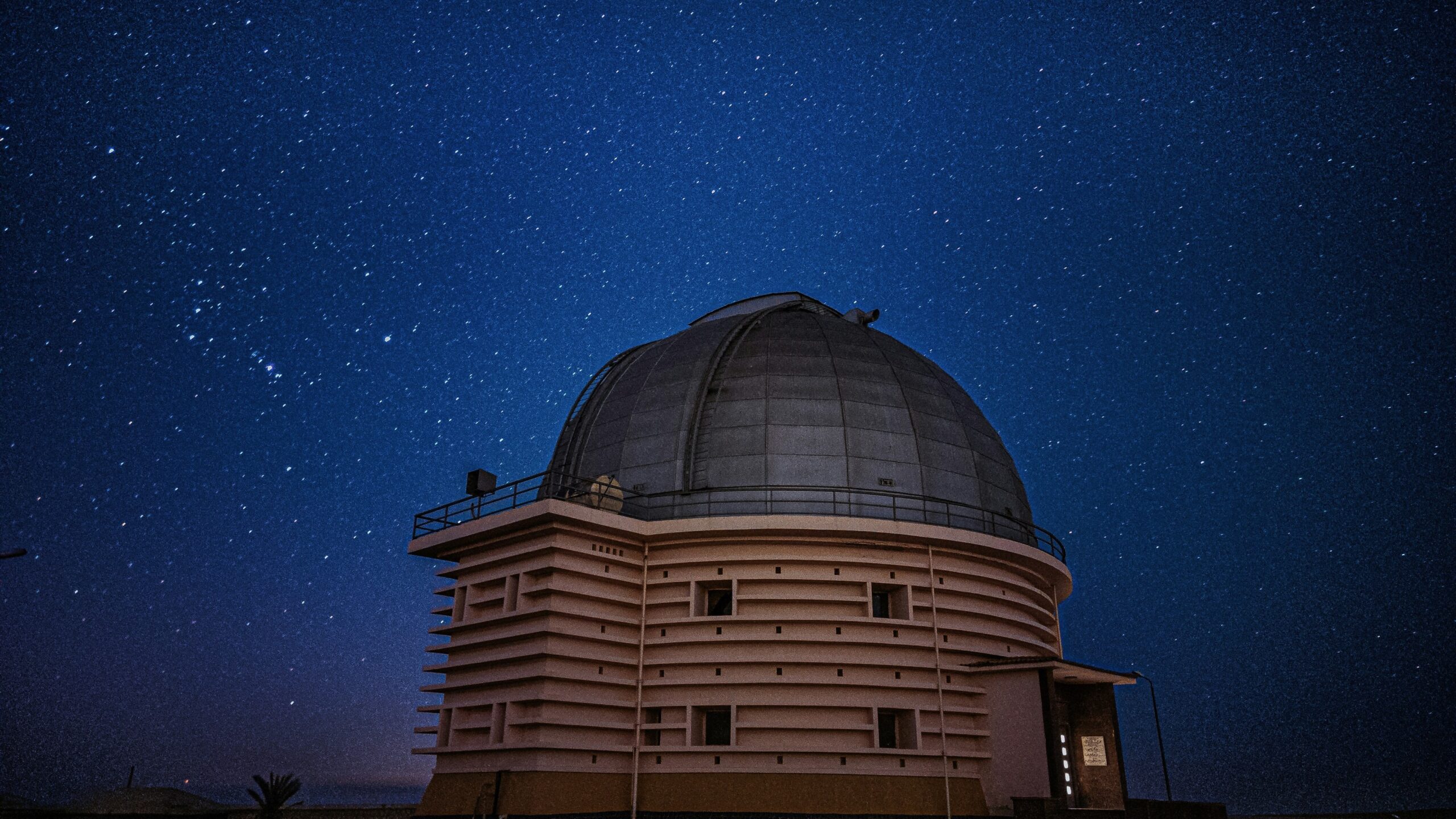 Astronomical observatory with a large dome under a clear night sky filled with stars, photographed from ground level